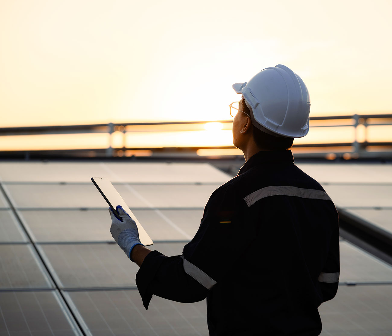 A man in a hard hat holding a tablet working on solar panels.