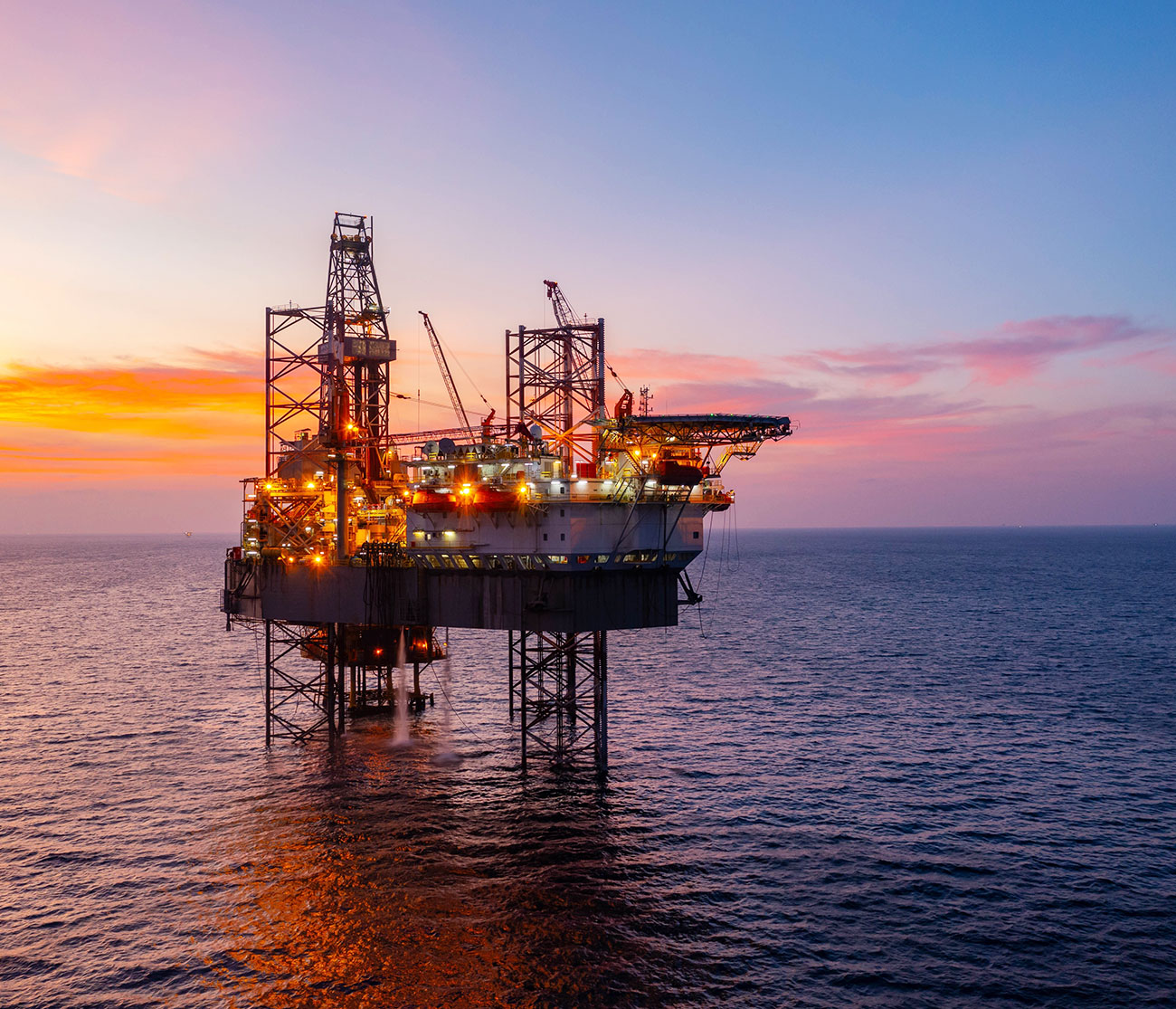 An oil rig in the middle of the ocean during sunset.