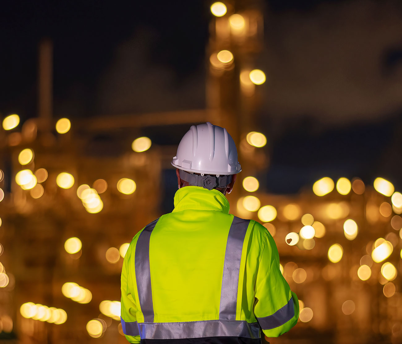 A man wearing a hard hat and reflective jacket at night.